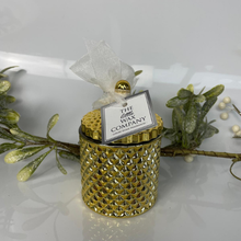 Decorative gold candle holder with a tag from 'The Little Wax Company' on a white background with greenery.