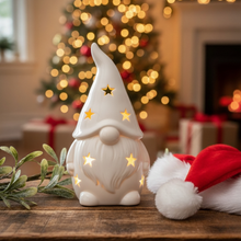 Decorative gnome with star lights on a wooden surface in a festive setting with a Christmas tree and presents.