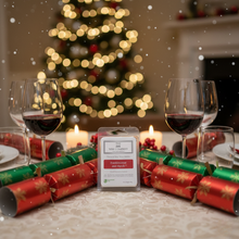 Christmas-themed table setting with wine glasses, crackers, and a lit candle in front of a blurred Christmas tree.