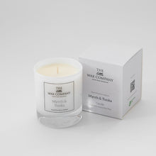 A small white candle with a label that reads 'Myrrh & Tonka' alongside a white box with the same label and brand, The Wax Company.