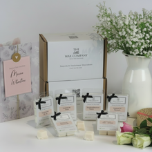 A collection of wax melt cubes from The Wax Company, displayed in front of their packaging. The cubes are white and there are labels in front of them with black text.