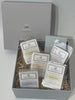 A gift box open to reveal multiple packaged wax melts with labels, accompanied by a bed of decorative straw. An additional pack of tea lights is also visible.