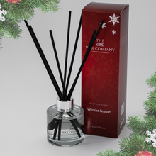 A clear reed diffuser bottle with black reeds and a silver cap, placed in front of a red and white Christmas-themed box with 'The Little Wax Company' branding.