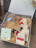 An open gift box displaying a clear wax burner and multiple wax melts with red ribbons. The gift box is presented on a neutral background.