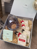 A gift box open to reveal a pearl grey wax burner, four wax melts, and additional complimentary wax melt and tea lights, all arranged on a bed of decorative straw. The gift box is adorned with red ribbon bows.
