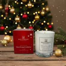 Candle and packaging from The Wax Company in front of a decorated Christmas tree.