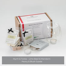 A gift set including a grey/blue glass tea light burner and three packs of luxury wax melts in different fragrance names displayed alongside a box with branding visible.