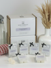A collection of wax melt cubes from The Wax Company, displayed in front of a box with cleaning fragrances. The cubes are labeled with different scent names and are presented with a vase of dried plants and cleaning supplies in the background.