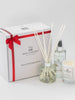 A luxury gift box set containing a white classic candle, a reed diffuser, and a room spray, all tied with a red ribbon.